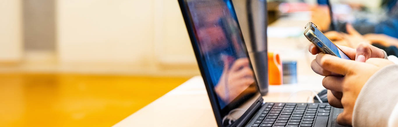 Jongen achter laptop met smartphone in hand