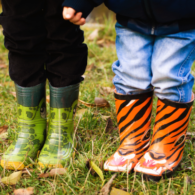 Twee kinderen, je ziet alleen de benen in regenlaarzen op een grasveld met balderen