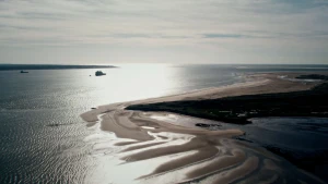 Een foto van de Waddenzee bij laag water. Op de achtergrond varen er twee schepen.