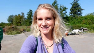 Een foto van presentator Janouk genomen op een betegelde straat met op de achtergrond bomen, struiken en een kruiwagen zichtbaar.