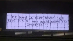 Een foto van een getypte tekst op een wit velletje op een voor het grootste deel zwarte achtergrond. De tekst is: "Dit bord is niet beveiligd! Stel z.s.m. een wachtwoord in! Groetjes".  Naast de tekst is een lachende emoticon getypt.