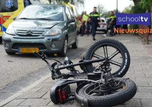 Een op de grond gevallen fatbike met een auto, politie en ambulance erbij. Er is duidelijk sprake van een ongeluk, maar je ziet geen gewonden.