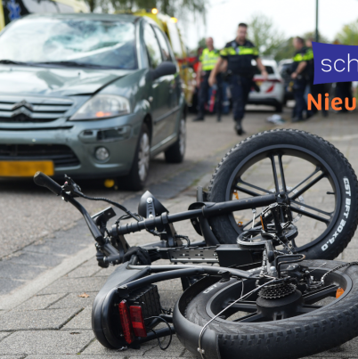 Een op de grond gevallen fatbike met een auto, politie en ambulance erbij. Er is duidelijk sprake van een ongeluk, maar je ziet geen gewonden.