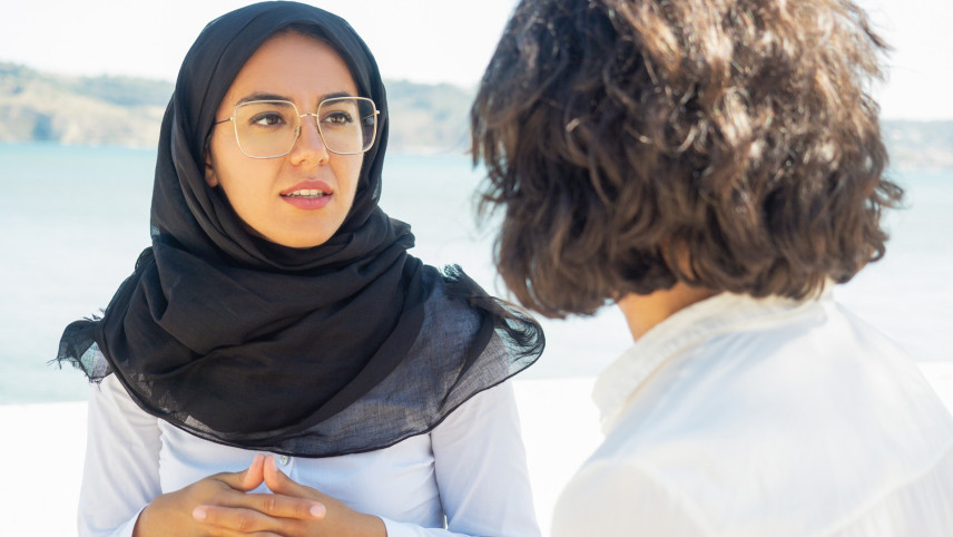 Twee vrouwen in gesprek, een van hen draagt een zwarte hoofddoek en een bril.