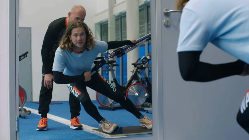 Een foto van presentator Pascal die in een sportschool aan het trainen is. Er staat een trainer achter hem.