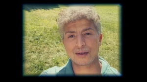 Een foto van het gezicht van een presentator die op een grasveld staat en veel ouder lijkt op de foto dan hij is. Dit komt doordat hij een 'ouder lijken' functie van een app op zijn mobiele telefoon gebruikt om de foto te nemen.