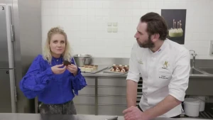 Een foto van presentatrice Janouk en bakker Hidde in de keuken. Janouk proeft de chocoladetaart die ze samen met bakker Hidde gemaakt heeft.