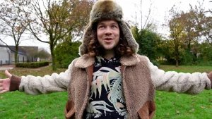 Foto van presentator Pascal die buiten staat op een grasveld en een winterjas en Russische bontmuts draagt.