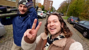 Presentator staat op straat met de cameraman en steekt twee vingers omhoog.