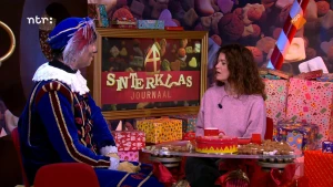 Foto van Piet aan tafel met presentatrice Merel voor een Sinterklaas decor.