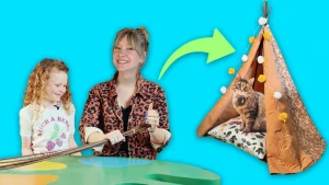 Een vrouw en een kind zitten aan een tafel en rechts daarnaast een kat in een tipitent.