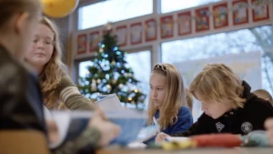 Een foto van kinderen aan tafel op school. Vier kinderen zijn te zien. Ze zitten in een klaslokaal aan tafel en zijn gefocust bezig met hun rekenwerk. Er is een kerstboom op de achtergrond te zien, met lichtjes erin.