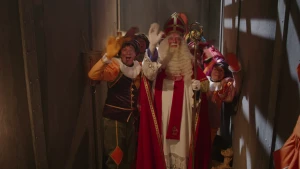 Sinterklaas en een aantal pieten staan in een gang op de stoomboot en zwaaien naar de camera.