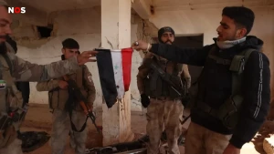 Een foto van mensen in legerkleding met geweren. Twee mensen houden een brandende Syrische vlag vast.