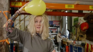 Foto van presentatrie Janouk die gele ballon over haar haar wrijft waardoor het overeind gaat staan.