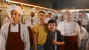 Foto van groep mensen met bakkerskleding aan en in het midden twee normaal gekleedde kinderen, hoofdpersoon Hein en vriendin Dewi die vol verwachting kijken.