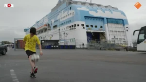 Foto van een jongen die de bal hooghoudt aan de kade, met daarachter een cruiseschip zo groot als een appartementengebouw.