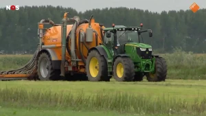 Foto van een tractor met een een grote mestverspreider eraan gekoppeld. De tractor rijdt over een grasveld.