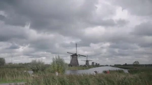 Foto van een kanaal met dijken waar oude windmolens opstaan. De lucht is donker bewolkt.