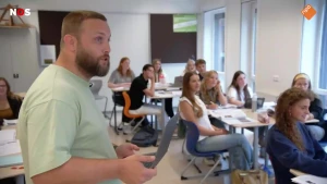 Foto van docent met laptop in de hand die voor de klas staat met oudere tieners die zitten.