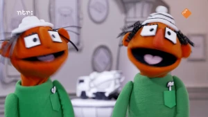 Foto van twee oranje poppen die lachen. Ze hebben allebei een witte muts  en groene trui.