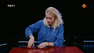 Foto van presentatrice Janouk die aan tafel zit en met een tangetje in de weer is. 