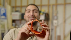 Een foto van Nizar die een oranje papier voor de camera houdt, dat gevouwen is in de vorm van een cirkel. 