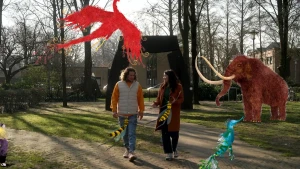 Foto van kunstenaar Djenné Fila en presentator Pascal die pratend wandelen door een bos. Er zijn illustraties van een mammoet en een vliegend sprookjesdieren over het beeld.