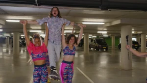 Foto van presentator Pascal op rolschaatsen die wordt opgetild door twee vrouwen in een parkeergarage.