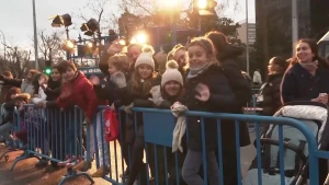 Er zijn op deze afbeelding kinderen te zien die achter dranghekken staan in Spanje bij de Driekoningen optocht. De kinderen zijn vrolijk en zwaaien.