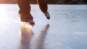 Foto van iemand die schaatst op natuurijs, ondergaande zon op de achtergrond.