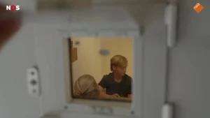 Foto van een celdeur waar je door het raampje twee kinderen ziet zitten.