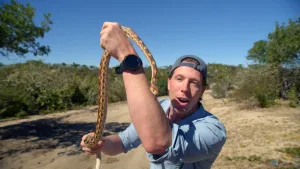 Foto van Freek Vonk die vertelt over een lange slang die hij in zijn handen vasthoudt.