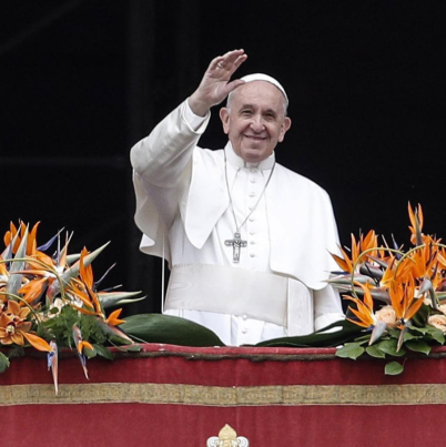 Een foto van de glimlachende en in het wit geklede paus Fransiscus die vanaf zijn versierde balkon zwaait