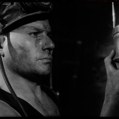 Zwartwitfoto van mijnwerker die naar mijnlamp kijkt.