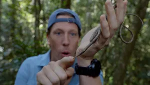 Een foto van Freek Vonk die een slang die op een liaan lijkt in zijn hand houdt en ernaar wijst.