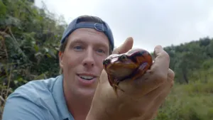 Een foto van Freek Vonk die glimlachend een kikker in zijn hand vasthoudt.