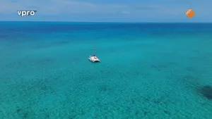 Een foto van een felblauwe zee met een dobberende witte zeilboot.