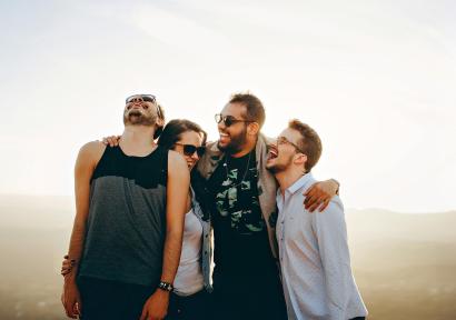 Foto van vier lachende jonge mensen met armen om elkaar heen.