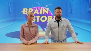 Foto van presentatoren Janouk en Job die naast elkaar staan en de camera inkijken. Janouk legt uit en Job kijkt moeilijk en vertwijfeld.