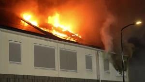  Een foto van een gebouw waar de vlammen uit het dak komen en dikke zwarte rook uit een raam.