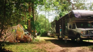 Een foto van een cmaping met links een tent en rechts een camper waar net iemand uit stapt.