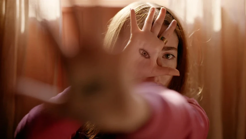 Een close-up foto van een meisje met een hand voor zich uit en een hand voor haar gezicht, op die hand is een oog getekent.