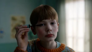 Een foto van een kind dat mascara op doet, terwijl het in de camera kijkt.