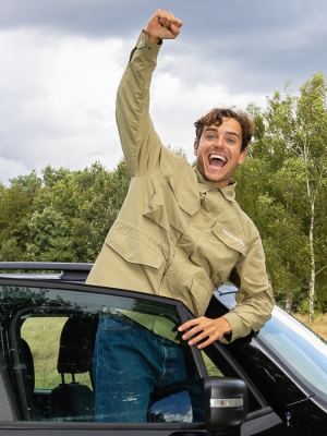 Een foto van presentator Floris die in zijn auto staat met een vuist gebald in de luhct en een lachend gezicht.