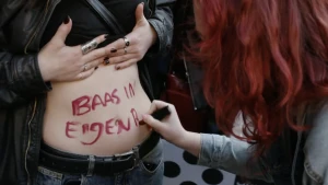 Foto van een vrouw die 'baas in eigen buik' schrijft op de buik van een andere vrouw