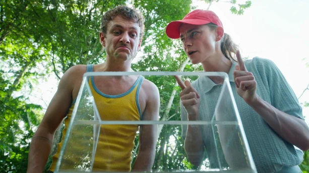 Een foto van beide presentatoren die in een glazen bak kijken, Jurre kijkt bedenkelijk, Emma vastberaden.