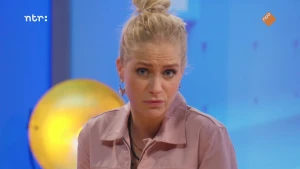 Een foto van presentatrice Janouk voor een blauwe achtergrond met een gele lamp of bal.