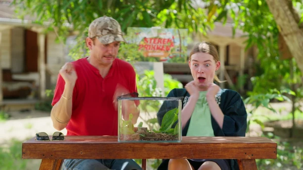 Een foto van presentatoren Jurre en Emma die geschrokken kijken naar een glazen bak die voor hen op tafel staat.