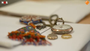 Foto van een antiek horloge en een broche op een bureau met documenten.